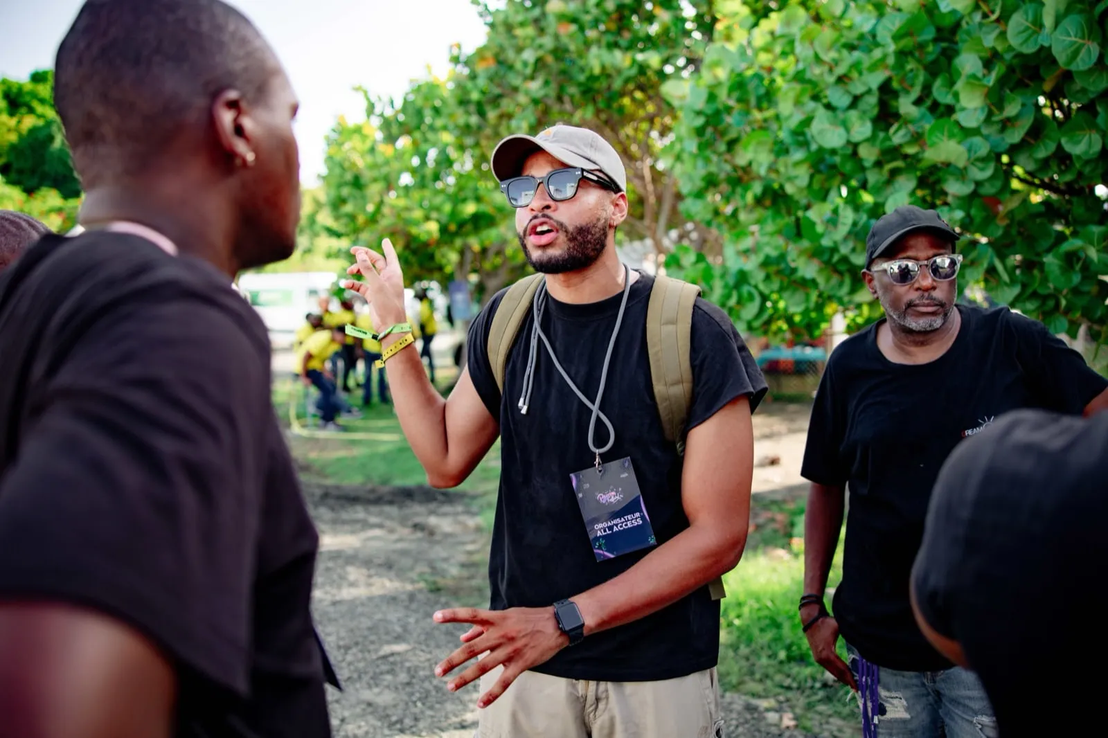 Swan Badol, badge d'organisateur au cou, en train de briefer trois personnes sur le site d'un festival.