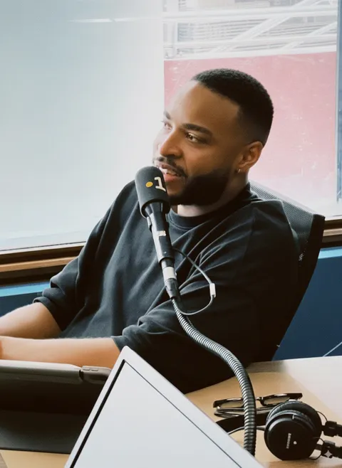 Swan Badol au micro dans un studio de radio, casque et écrans devant lui.